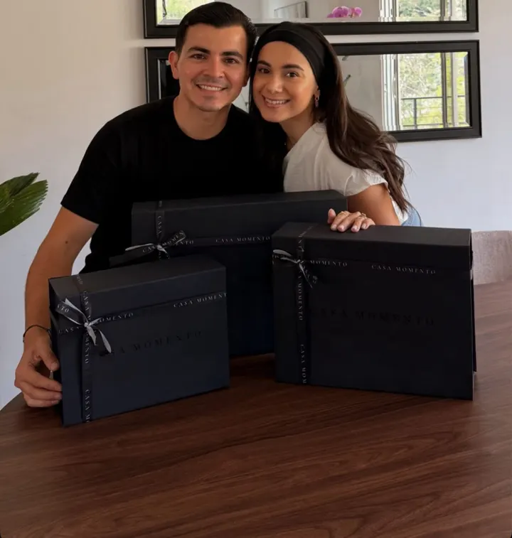 Gustavo y Pamela sonriendo detrás de tres cajas negras con listón de Casa Momento